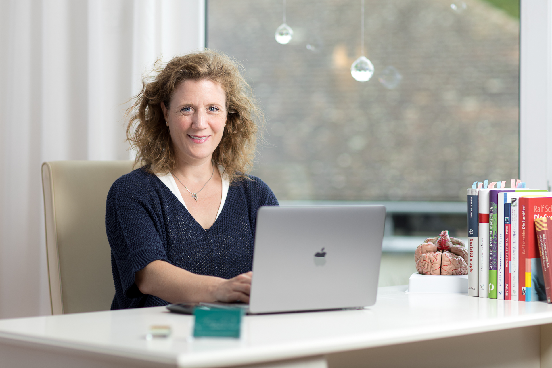 Christina Isabelle Löhnert sitzt am Schreibtisch ihrer Praxis mit geöffnetem MacBook  bei der Online-Therapie